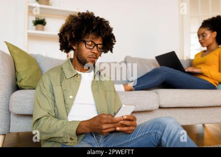 Man Using Smartphone While Wife Browsing Internet On Computer Indoor Stock Photo