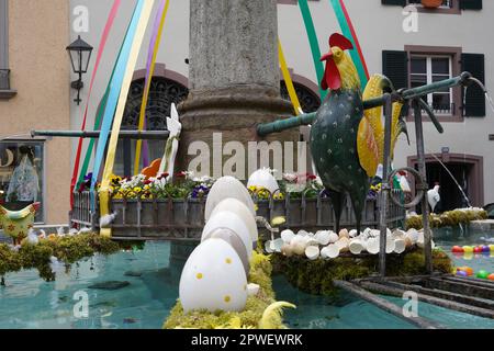 Outdoor Easter decoration in a fountain. There is a row of Easter eggs on the water, heap of egg shells and a rooster on the background. Stock Photo
