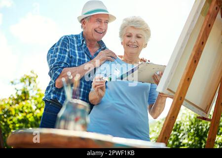 Keeping her shoulders nice and loose as she paints. a senior couple painting in the park. Stock Photo