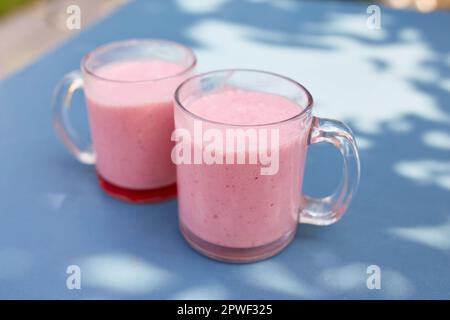 Two pink fruit and milkshakes in glass cups stand on a table in a cafe on the street Stock Photo
