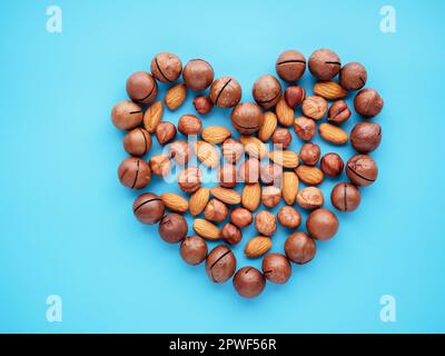 Various organic nuts forming heart shape on blue background. Tasty macadamia, hazelnut and almond. Top view and copy space. The concept of health care Stock Photo