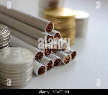 Money in coins and cigarettes in bulk as a symbol of increasing prices for cigarettes Stock Photo