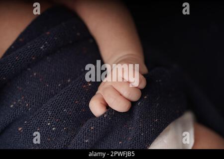 Tiny baby hands holding navy blue blanket. close-up view of the baby's cute hand the baby is laying comfortably in a blue blanket. Stock Photo