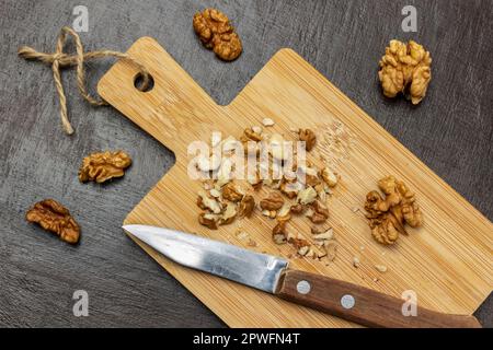 Crushed walnuts and knife on cutting board. Walnut shell and walnut kernels on the table. Flat lay. Brown background. Stock Photo