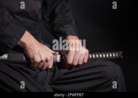 The samurai holding a Japanese katana sword. Photo of a warrior dressed in black clothes in low key with selective focus Stock Photo