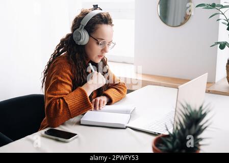 Young woman elearning from home, attending virtual class and remote conference meetings on laptop. Female student distance learning at home with Stock Photo