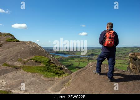 Man looking over Tittesworth reservoir walking backpacking on Hen Cloud rocks part of the Roaches Ridge in the Peak District  Stafordshire Moorlands Stock Photo