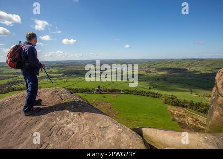 Man looking over Tittesworth reservoir walking backpacking on Hen Cloud rocks part of the Roaches Ridge in the Peak District  Stafordshire Moorlands Stock Photo