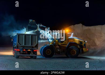 Heavy construction and mining machinery loading a dump truck with gravel in a quarry on the night shift. Close-up. Stock Photo