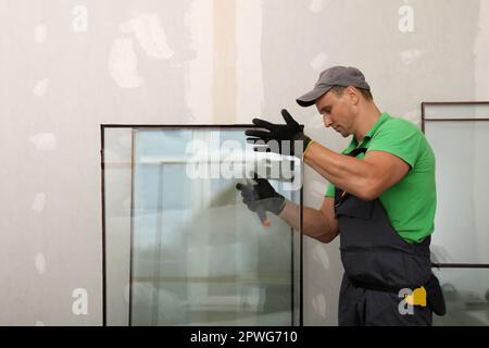 Worker in uniform preparing double glazing window for installation indoors Stock Photo