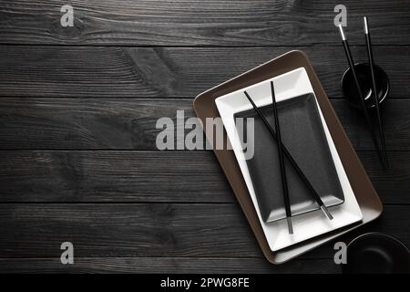 Stylish sushi dishware and chopsticks on black wooden table, flat lay. Space for text Stock Photo