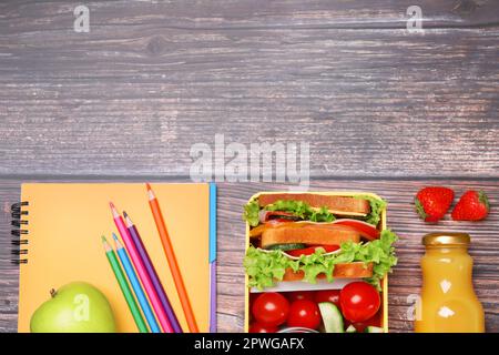 Lunch box with healthy food and different stationery on wooden table, flat lay. Space for text Stock Photo