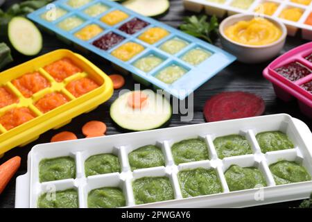 Different frozen purees in ice cube trays and ingredients of black wooden table. Ready for freezing Stock Photo