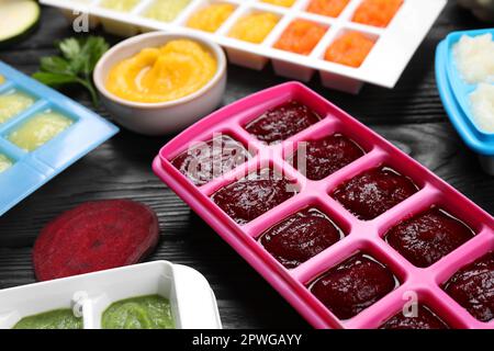 Different frozen purees in ice cube trays and ingredients of black wooden table. Ready for freezing Stock Photo