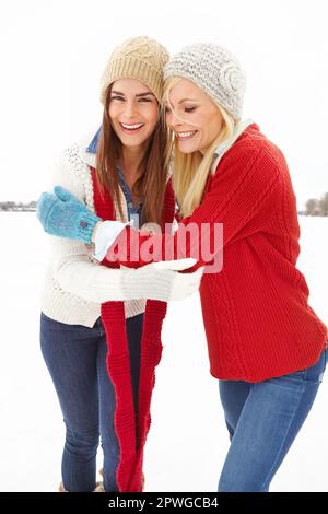 Warmth can be your greatest asset. Portrait of two friends standing in the snow together keeping each other warm. Stock Photo