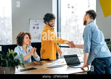 Handshake. Businesspeople signed a cooperation agreement, make a deal. Friendly male successful partners shake hands to each other in a boardroom, smile, satisfied with successful negotiations Stock Photo