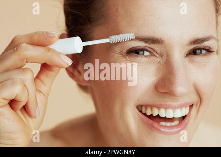 smiling middle aged woman with brow brush on beige background. Stock Photo