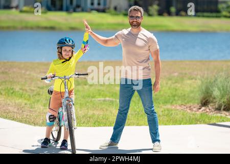 Father and son learning to ride a bicycle having fun together at Fathers day. Father teaching his son cycling on bike in american neighborhood. Father Stock Photo