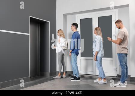 Group of people waiting in line for elevator while woman pressing call button Stock Photo