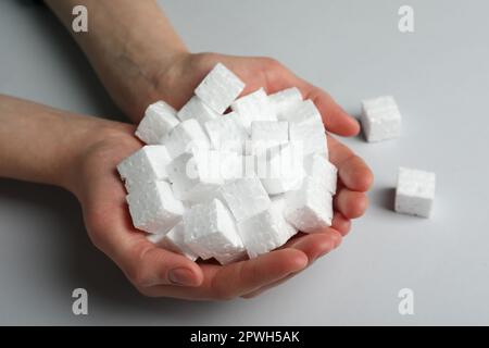 Woman with handful of styrofoam cubes on light grey background, closeup Stock Photo