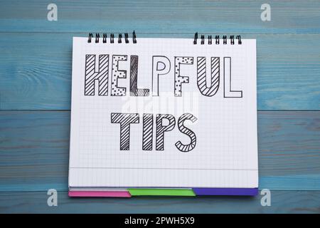 Phrase Helpful Tips in notebook on light blue wooden table, top view Stock Photo