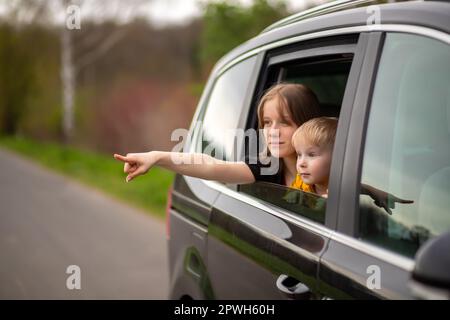 Happy brother and sister looking out car window , point the finger to the side and look in surprise Stock Photo