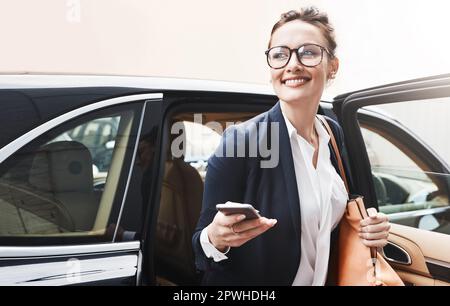 Finally at work. a cheerful young businesswoman getting out of a car while holding a cellphone outside during the day. Stock Photo