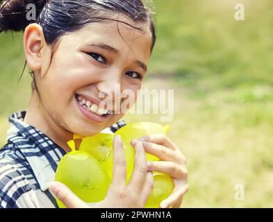 All smiles she got all the water balloons. Portrait of an adorable little girl playing with water balloons outdoors. Stock Photo