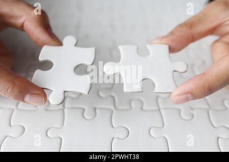 Business woman hand is trying to connect couple White jigsaw puzzle piece on a blue background. Symbol of association and connection. Concept of busin Stock Photo