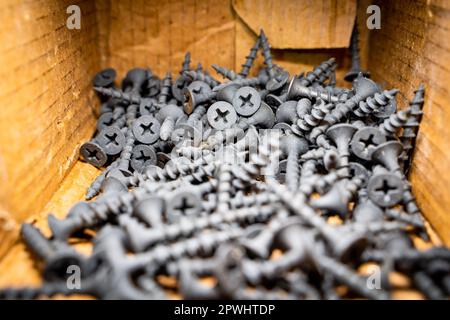 Small black wood screws close-up in a cardboard box Stock Photo