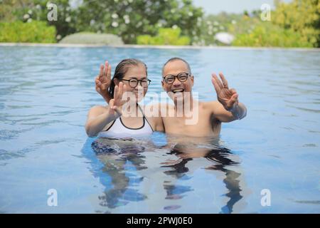 asian couple raising three finger with relaxing in swimming pool Stock Photo