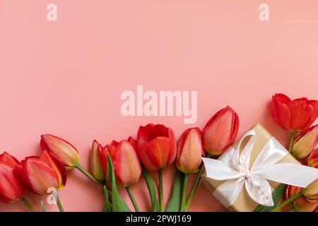 Gift box with red tulips on pastel pink background with empty space. Mother's Day, wedding, valentines day celebration concept. View from above. Stock Photo