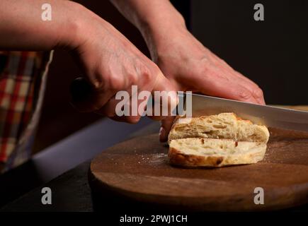 The healthy eating and traditional bakery concept. Front viev. Whole grain bread put on kitchen wood plate with a chef holding knife for cut. Fresh br Stock Photo