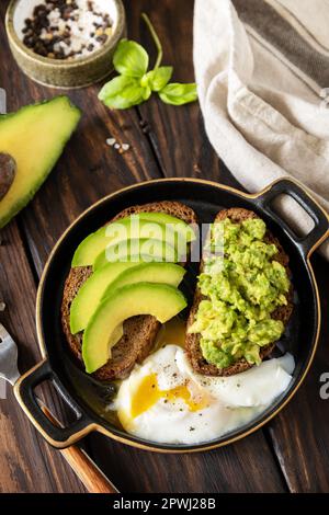 Healthy breakfast, sandwich with avocado and egg. Wholemeal bread toast sliced avocado and poached egg on a rustic table. Stock Photo
