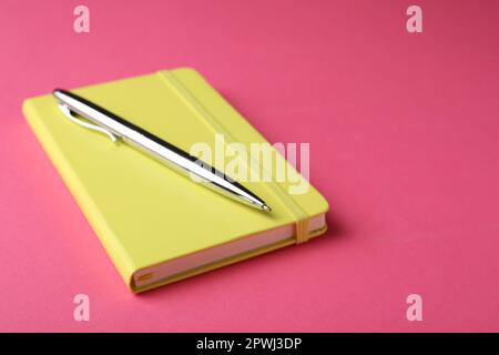 New stylish planner with hard cover and pen on pink background. Space for text Stock Photo