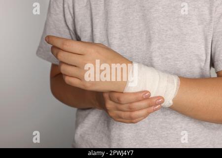 Doctor wrapping bandage around young woman's chest on white background,  closeup Stock Photo