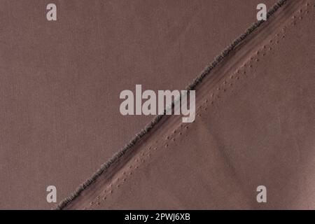 Straight undone seam of brown fabric by torn edge of cloth Stock Photo