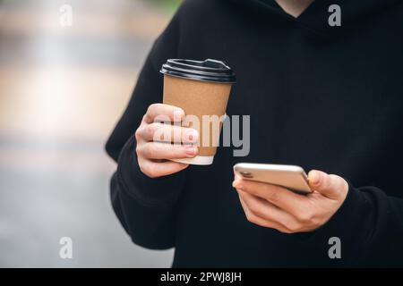 Man holding paper cup and smartphone outdoors. Stock Photo