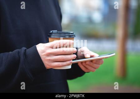 Man holding paper cup and smartphone outdoors. Stock Photo
