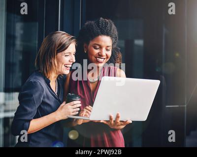 Working hard and having fun along the way. two young businesswomen using a laptop outside an office. Stock Photo