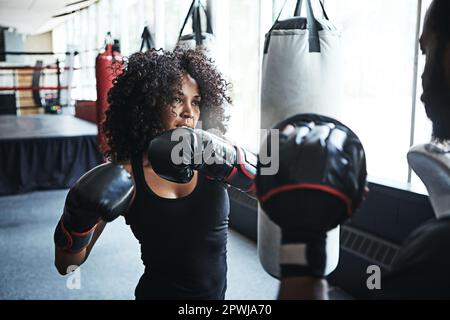 Every move you make starts with your heart. a female boxer practising her moves with her coach. Stock Photo