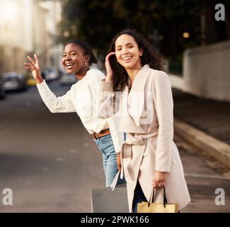 hang on sale, were on our way. two young women calling a cab after shopping against an urban background Stock Photo