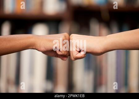 Were going to achieve great things. two unrecognizable people giving each other a fist bump in a library at college Stock Photo