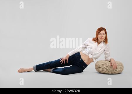Barefoot middle age woman leaning on padded stool. Studio concept of carefree life. Stock Photo