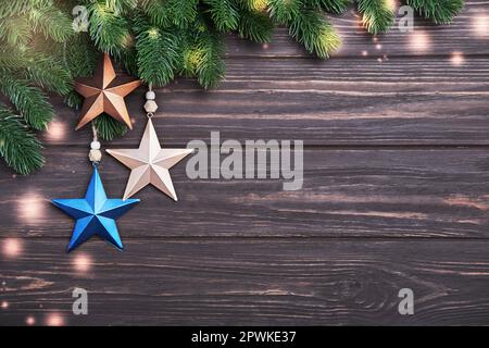 Christmas or New Year background with fir branches and decorations in form of star on a wooden backdrop. Happy Holidays concept in minimalistic style. Stock Photo