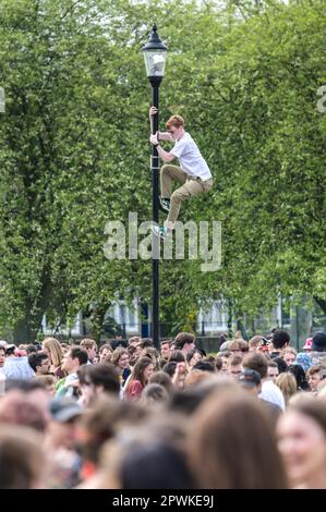 Jesus Green, Cambridge, 30th April 2023 - A lad climbed a lamppost as hordes of Cambridge University students flocked to a park on Sunday afternoon in the Bank Holiday sunshine for the annual 'Caesarian Sunday' drinking party. Undergraduates from the prestigious institution frolicked through the afternoon in fancy dress taking part in drinking games on Jesus Green. The tradition, also known as ‘C-Sunday' attracts thousands of students just before they take part in exams. Police were present to keep the academics in check. Credit: Ben Formby/Alamy Live News Stock Photo