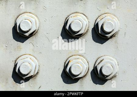 Six large nuts and bolts on gray steel plate of rail bridge, lit by bright sun. Abstract industrial background. Stock Photo