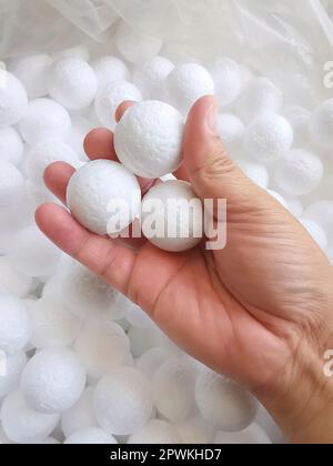 Hand holding white polystyrene foam beads ball drop from Styrofoam machine for fragile stuff packaging box on blue modern luxury background for decora Stock Photo