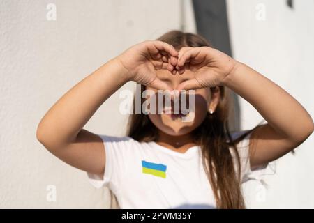 girl with flag of Ukraine on t-shirt showing a heart from the hands. Stop war Stock Photo