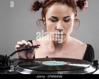 Beautiful woman about to put the needle down on the vinyl record spinning on her record player. Stock Photo